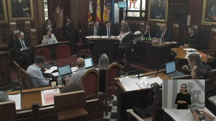 La regidora de Unidas Podemos en el Ayuntamiento, Lucia Muñoz, le entrega el chandal con el que fue deportada a España desde Israel al alcalde de Palma, Jaime Martínez, durante el pleno de este jueves.