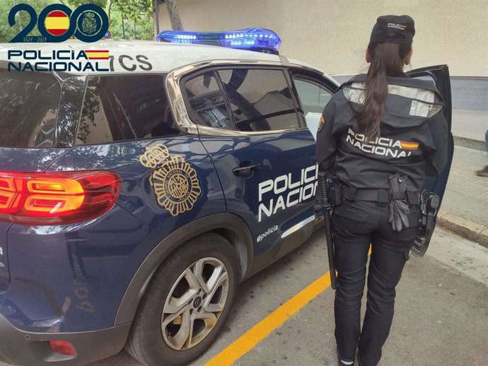 Una agente de la Policía Nacional de espaldas, junto a un vehículo policial. Recurso.