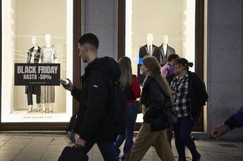 Archivo - Varias personas pasan por delante de los comercios que anuncian los descuentos del Black Friday 