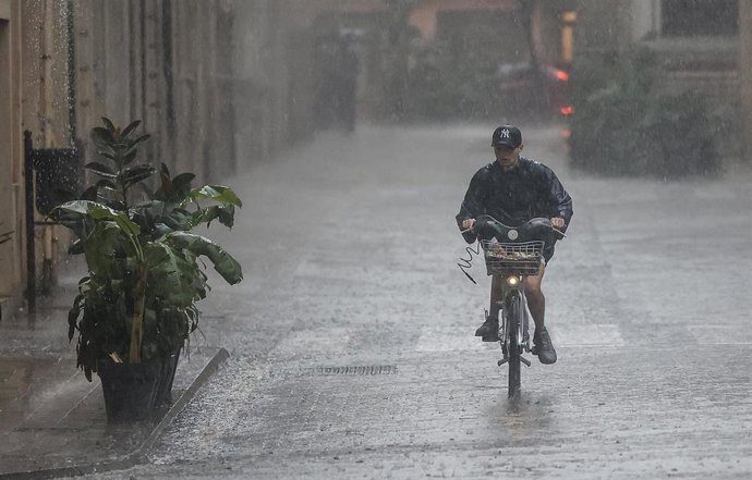 Archivo - Una persona en bicicleta bajo la lluvia.