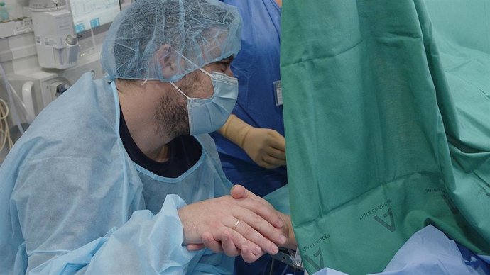 Un hombre coge la mano de su pareja mientras le practican la cesárea.