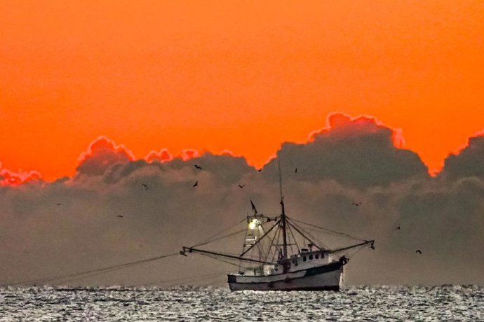 October 16, 2025, Isle Of Palms, Sc, United States: A shrimp trawler drags the coastline as the sun begins peaking up over a low bank of clouds on the Atlantic Ocean along Front Beach, October 16, 2025 in Isle of Palms, South Carolina.