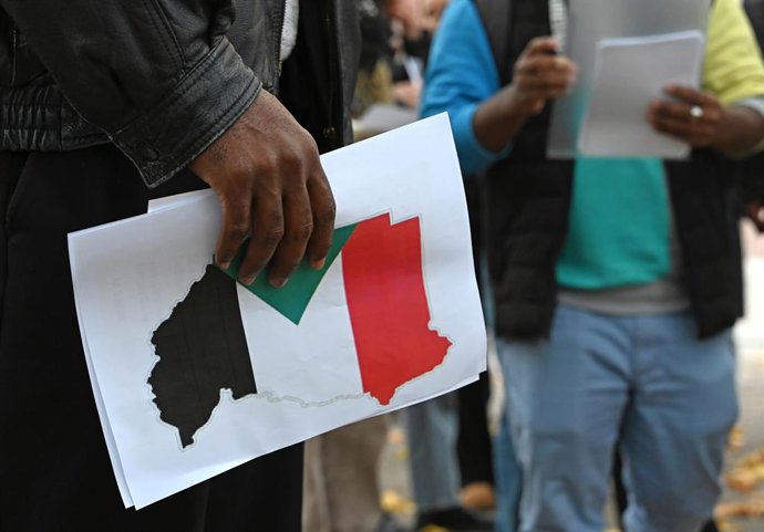 31 October 2025, Berlin: A person holds a flyer with the Sudanese flag during a vigil under the motto "Stand with Sudan - Stop the massacres in Al-Fasher" in front of the Federal Foreign Office. Photo: Elisa Schu/dpa