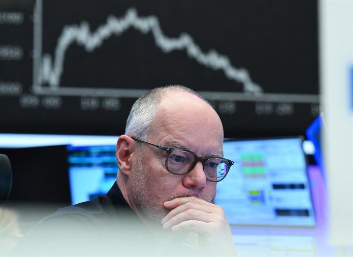 Archivo - 03 April 2025, Hesse, Frankfurt/Main: A stock market trader watches his monitors on the trading floor of the Frankfurt Stock Exchange as the display board with the DAX curve shows falling prices.