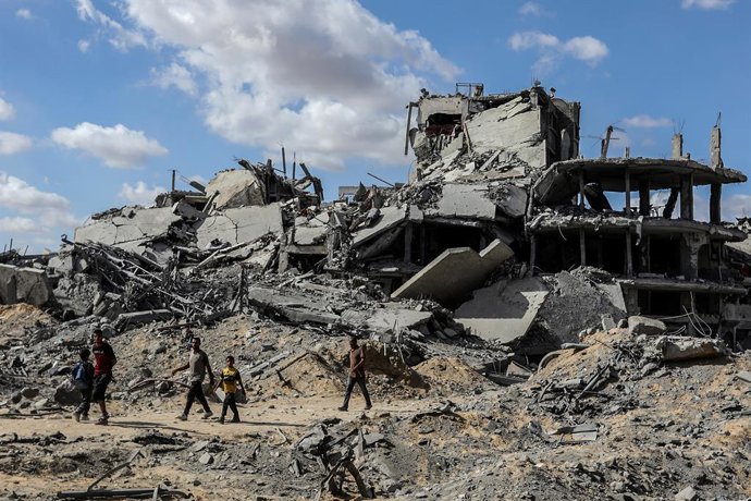 Archivo - FILED - 10 de outubro de 2025, Territórios Palestinos, Khan Yunis: Pessoas passam por prédios destruídos enquanto palestinos deslocados voltam para suas casas depois que o exército israelense se retirou de algumas áreas a leste de Khan Yunis, no