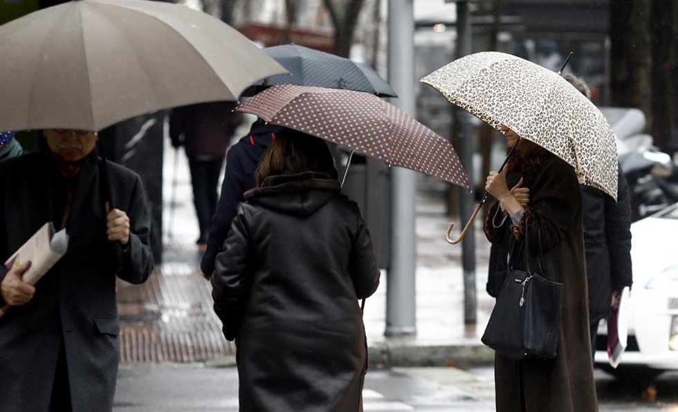 Archivo - Varias personas se protegen de la lluvia bajo un paraguas. Imagen de archivo