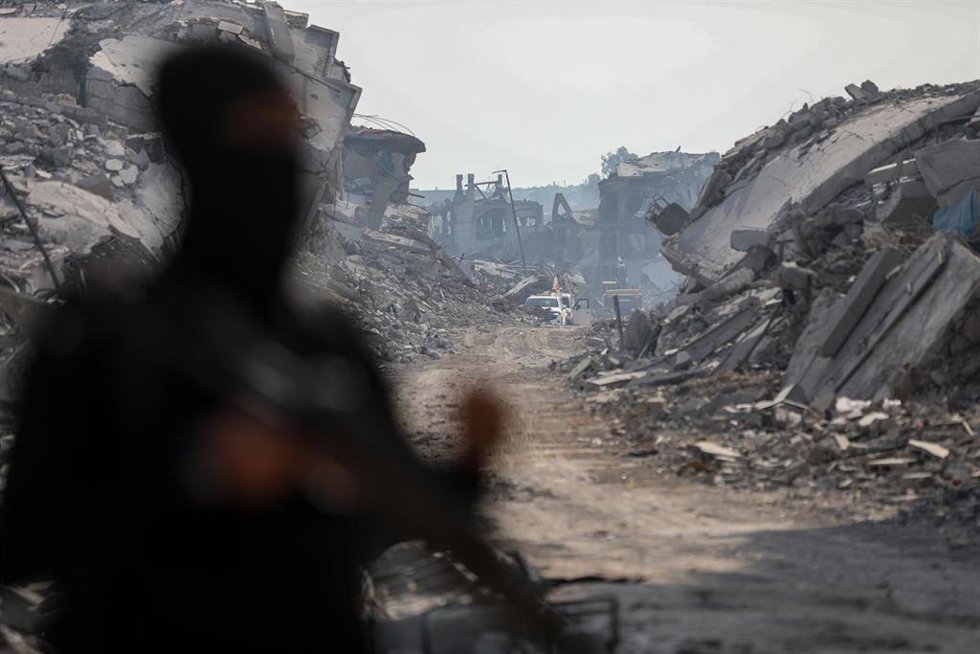 Archivo - Calles y edificios destruidos de fondo en la ciudad de Gaza, tras la figura de un combatiente de las brigadas Al Qassam, el brazo armado de Hamás