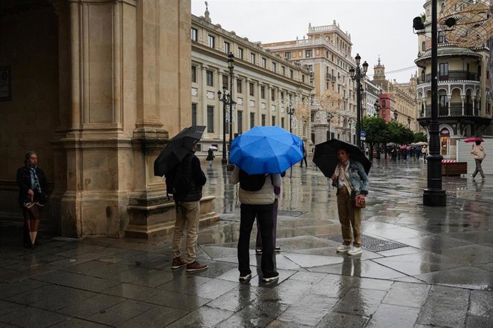 Sevillanos protegiéndose de la lluvia y el viento. Imagen de archivo.