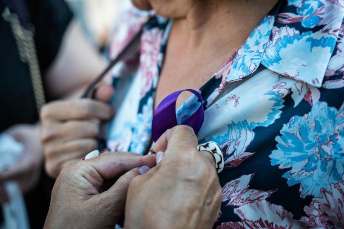 Archivo - Una mujer pone un lazo morado a otra