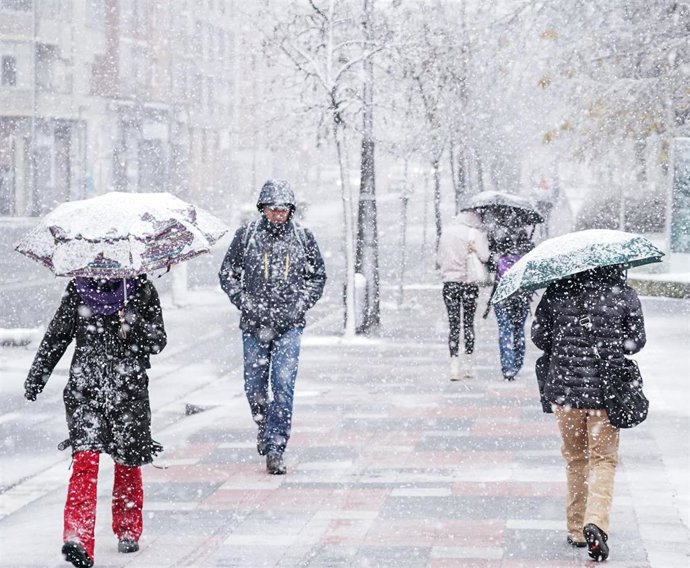 Archivo - Personas pasean bajo la nieve en Vitoria
