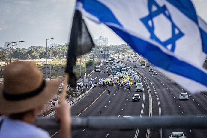 Archivo - Arquivo - 17 de agosto de 2025, Tel Aviv, Israel: Uma mulher israelense segura a bandeira de Israel enquanto está em uma ponte com vista para os manifestantes que bloqueiam a principal rodovia costeira. Eles pedem que o primeiro-ministro israele