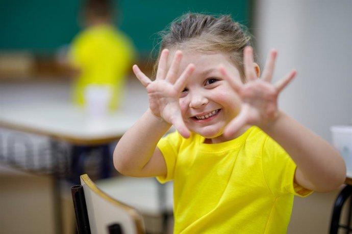 Archivo - Sonriendo niña en un aula mostrando sus manos y mirando a la cámara