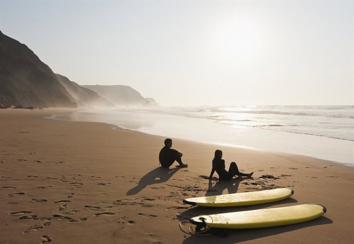 Archivo - Pareja de turistas descansando en una playa junto a unas tablas de surf