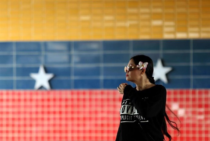 Archivo - Una mujer junto a un mural de la bandera venezolana en la ciudad de Valencia (Venezuela)