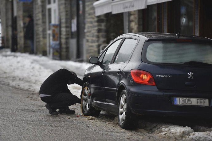 Archivo - Un hombre coloca cadenas en las ruedas de su coche