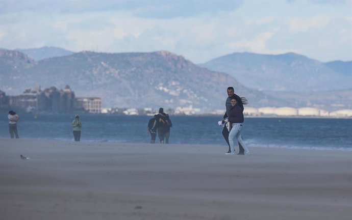 Archivo - Arxiu - Diverses persones caminen per la platja mentre els dona el vent