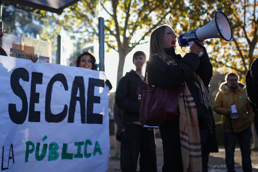Estudiantes protestan contra la "infrafinanciación" de las universidades y reparten folledos en una parada de autobús de Ciudad Universitaria.