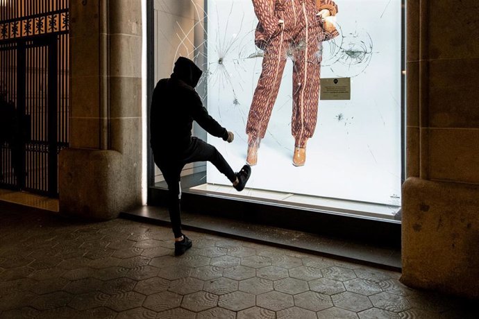 Archivo - Un joven da una patada contra el escaparate de una tienda durante una manifestación.