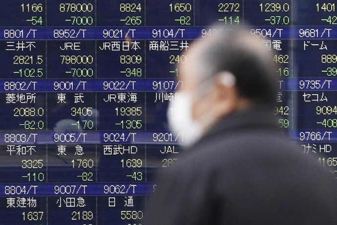 Archivo - 25 February 2020, Japan, Tokyo: A man wearing a surgical mask walks past an electronic stock board showing Japan's Nikkei Stock Average.