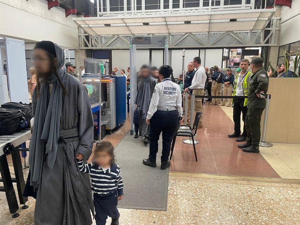 Un hombre de la secta judía Lev Tahor camina junto a una niña en un control de seguridad durante su traslado a Estados Unidos, tras la expulsión de Colombia de nueve adultos de la secta junto a 17 menores que serán entregados a los servicios sociales