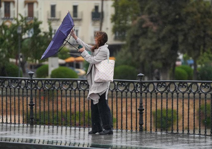 Imagen de archivo de sevillanos protegiéndose de la lluvia y el viento.