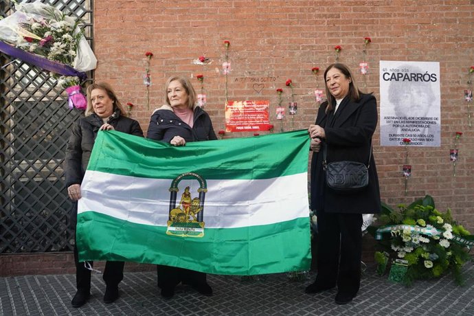 Paqui, Puri y Loli Caparrós posan con la bandera andaluza ante la placa homenaje que recuerda el lugar donde su hermano, Manuel José, murió asesinado el 4 de diciembre de 1977 durante una manifestación pro autonomía andaluza en la capital malagueña.