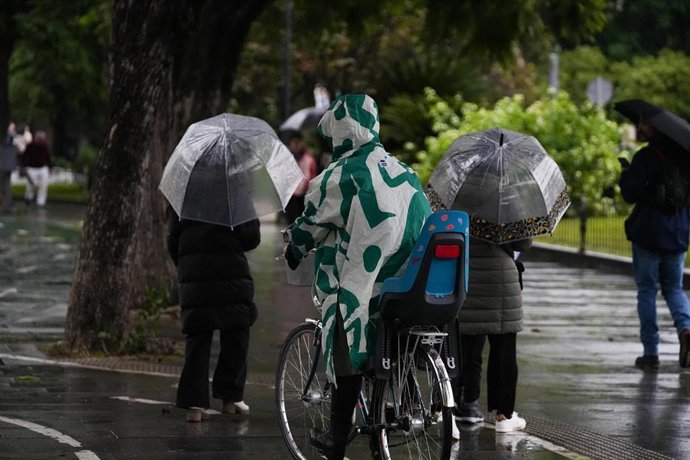 Viandantes protegiéndose de la lluvia y el viento. Imagen de archivo. 