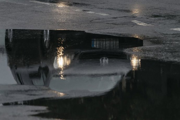 Archivo - Un coche reflejado en un charco circula bajo la lluvia, en imagen de archivo.