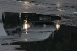 Archivo - Arxiu - Un cotxe reflectit en un toll circula sota la pluja, en imatge d'arxiu.