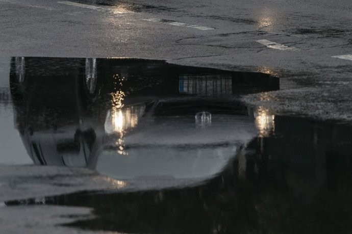 Archivo - Arxiu - Un cotxe reflectit en un toll circula sota la pluja, en imatge d'arxiu.