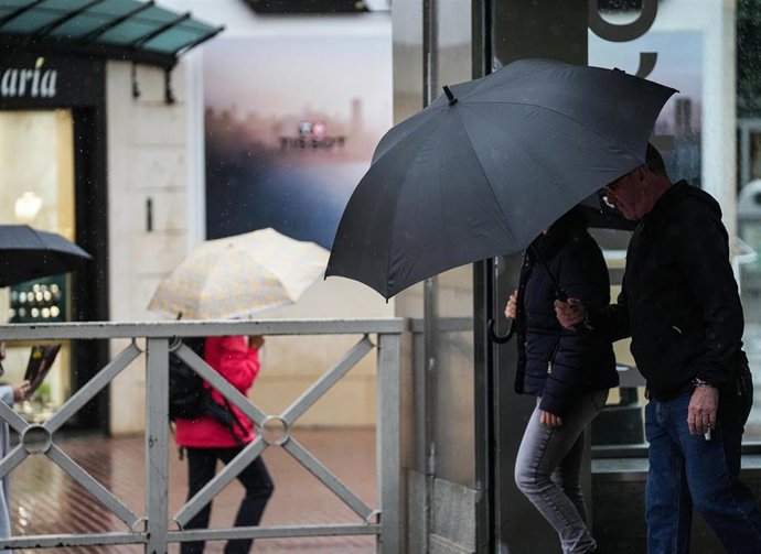 Sevillanos protegiéndose de la lluvia y el viento, protagonistas de la jornada de hoy con avisos naranja y amarillo en gran parte de Andalucía. A 13 de noviembre de 2025, en Sevilla (Andalucía, España). 