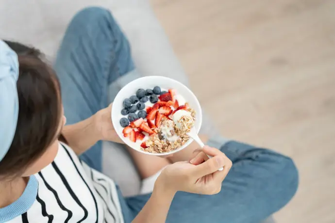 Mujer desayunando un cuenco de cereales y fruta