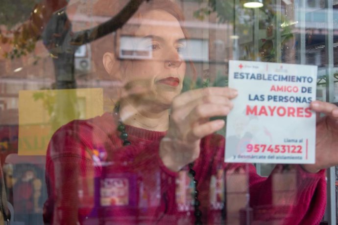 Una mujer coloca el cartel 'Establecimiento amigo de las personas mayores' en la ventana de un local.