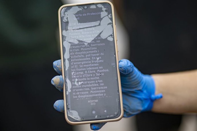 Archivo - Una mujer muestra la alerta de Protección Civil en su teléfono móvil en La Ràpita (Tarragona)