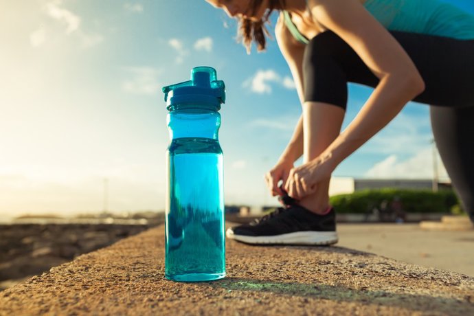 Archivo - Female runner tying her shoes next to bottle of water