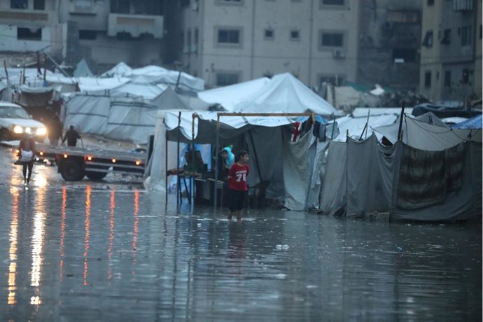 16 de dezembro de 2025, Cidade de Gaza, Faixa de Gaza, Território Palestino: Palestinos caminham sob a chuva em uma rua da Cidade de Gaza, cuja infraestrutura foi severamente danificada na recente guerra israelense. Uma tempestade que atingiu a Faixa de G