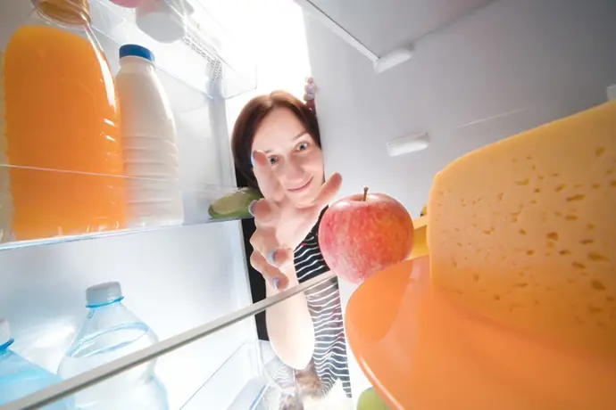Mujer abriendo la nevera: zumo de naranja, leche, agua, manzana, queso