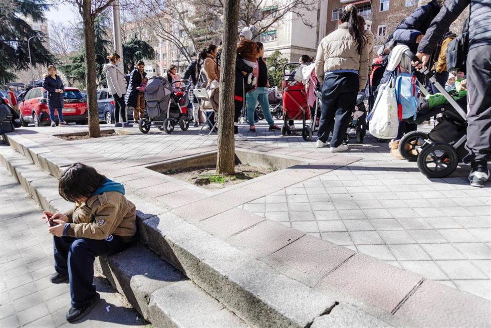 Archivo - Un grupo de persona espera una cola durante la entrega de ropa de abrigo y zapatos a familias vulnerables. 