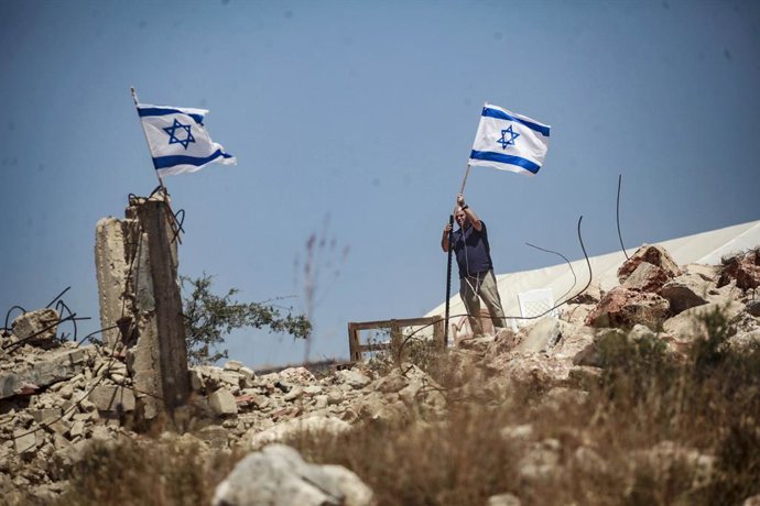 Archivo - Arquivo - 23 de maio de 2025, Salfit, Cisjordânia, Palestina: Um colono judeu levanta uma bandeira israelense em um terreno palestino perto de casas palestinas durante um ataque à cidade de Bruqin, perto da cidade de Salfit, no norte da Cisjordâ