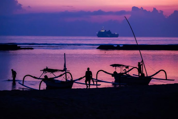 Archivo - Arxiu - FILED - 14 November 2022, Indonèsia, Nusa Dua: Men attach boats to the beach of Nusa Dua before sunrise on the day before the start of the G20 summit, with an Indonesian Navy ship visible in the background. Photo: Christoph Soeder/dpa