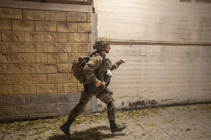 Archivo - 14 de junho de 2025, Israel, Tel Aviv: Um soldado israelense corre para o local de um ataque de míssil em Ramat Gan, perto de Tel Aviv, onde vários carros e edifícios foram destruídos. O ataque de 13 de junho foi parte de uma barragem de mísseis