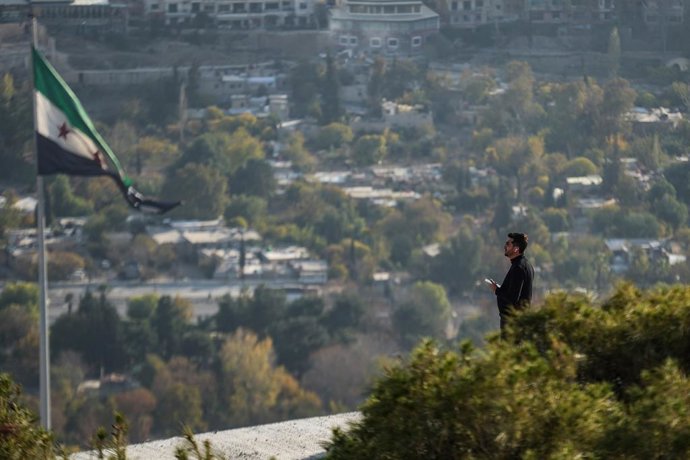 04 December 2025, Syria, Damascus: A man stands near a Syrian flag at an elevated viewpoint overlooking Damascus as the country approaches the first anniversary of the fall of Assad. Photo: Moawia Atrash/dpa