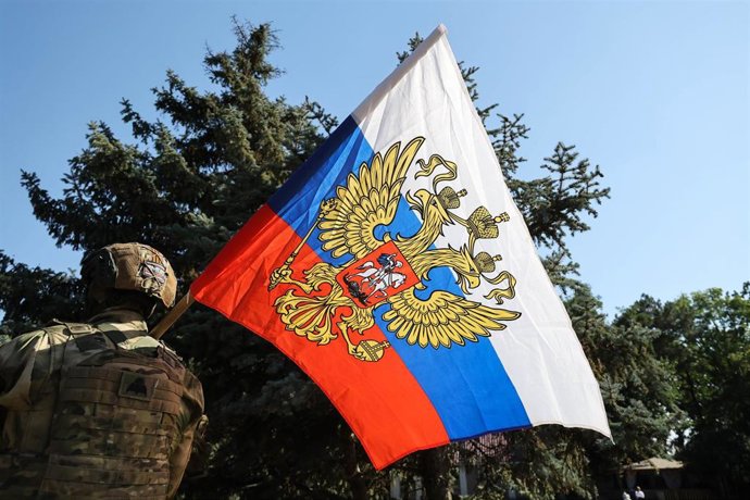 Archivo - Un oficial de la Guardia Nacional rusa sostiene una bandera rusa en una calle de Melitópol, Zaporiyia