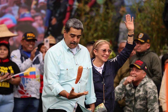 10 December 2025, Venezuela, Caracas: Venezuelan President Nicolas Maduro plays with a carrot next to his wife Cilia Flores (R)  Photo: Jesus Vargas/dpa