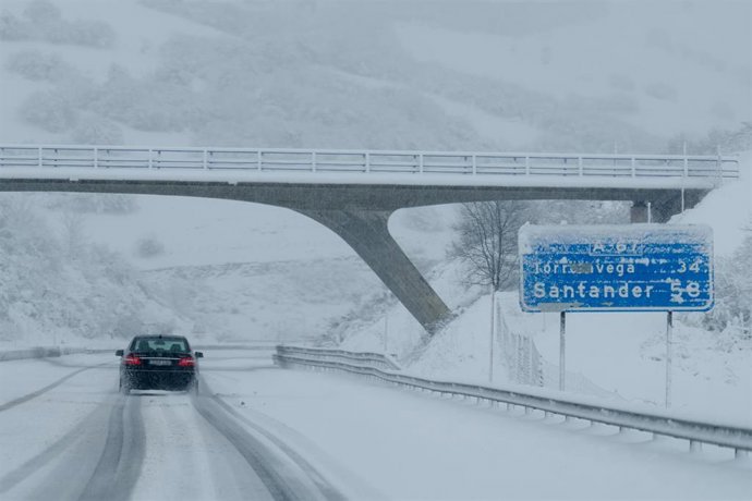 Archivo - Un coche conduce por una carretera cubierta de nieve en Cantabria.-ARCHIVO