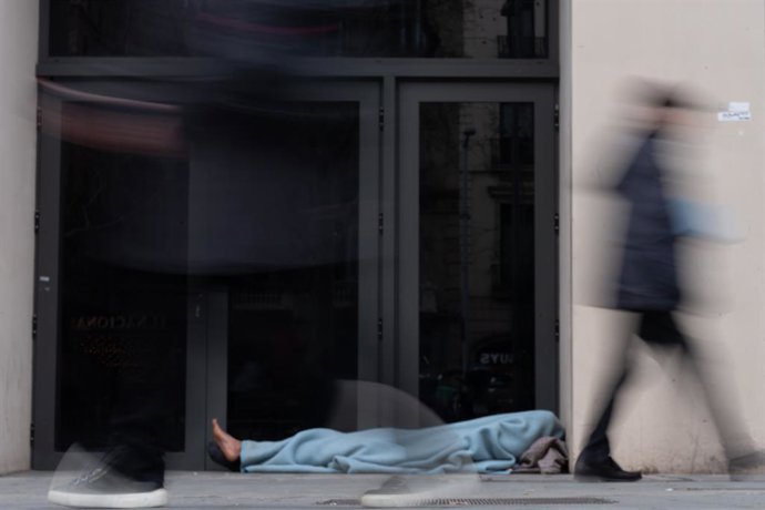 Archivo - Imatge d'arxiu - Diverses persones passen davant d'una persona sense llar, a Barcelona
