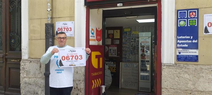 Víctor Sánchez, titular del estanco, posa junto al cartel con el número agraciado.