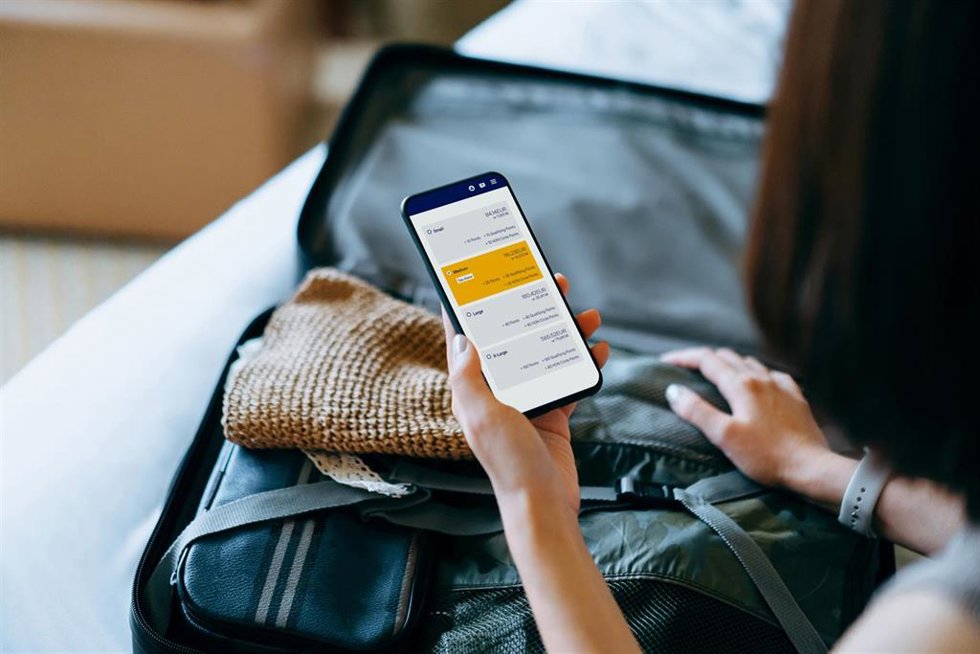 Archivo - Over the shoulder view of young Asian woman using smartphone, checking digital flight ticket and boarding pass on device screen while packing a suitcase on bed for a trip. Planning for travel. Travel and vacation concept