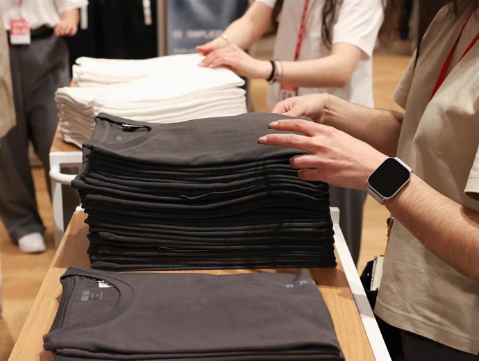 Archivo - Varios dependientes colocan la ropa en una tienda de moda