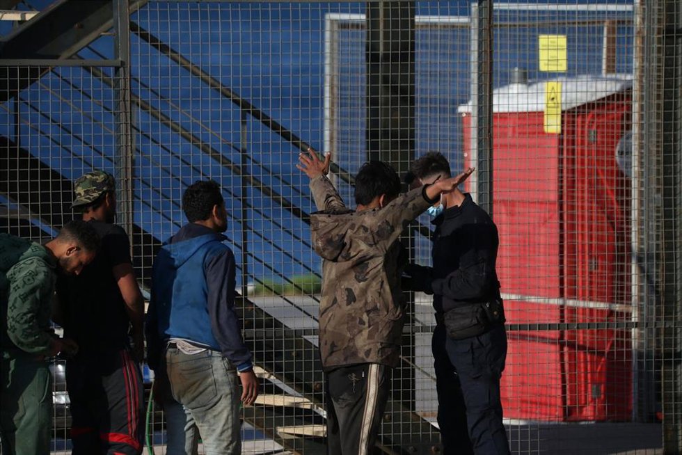 Archivo - Un guarda costero cachea a una persona migrante rescatada cerca de Creta y desembarcada en el puerto de Lavrio, en Atenas